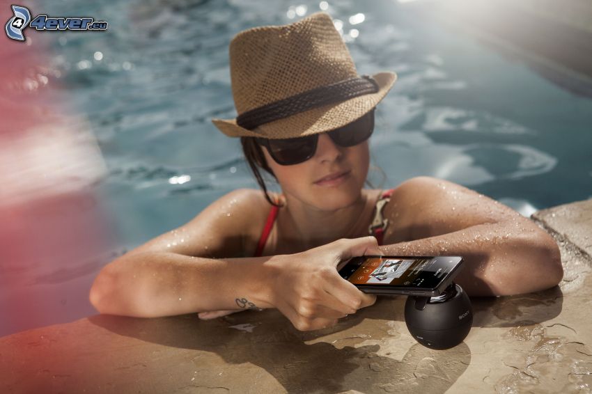 Frau im Swimmingpool, Handy, Hut, Sonnenbrille