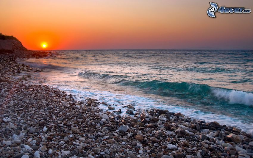 Sonnenuntergang auf dem steinigen Strand, Wellen an der Küste, Meer