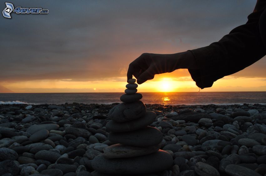 Steinstrand, Sonnenuntergang über dem Meer, Hand