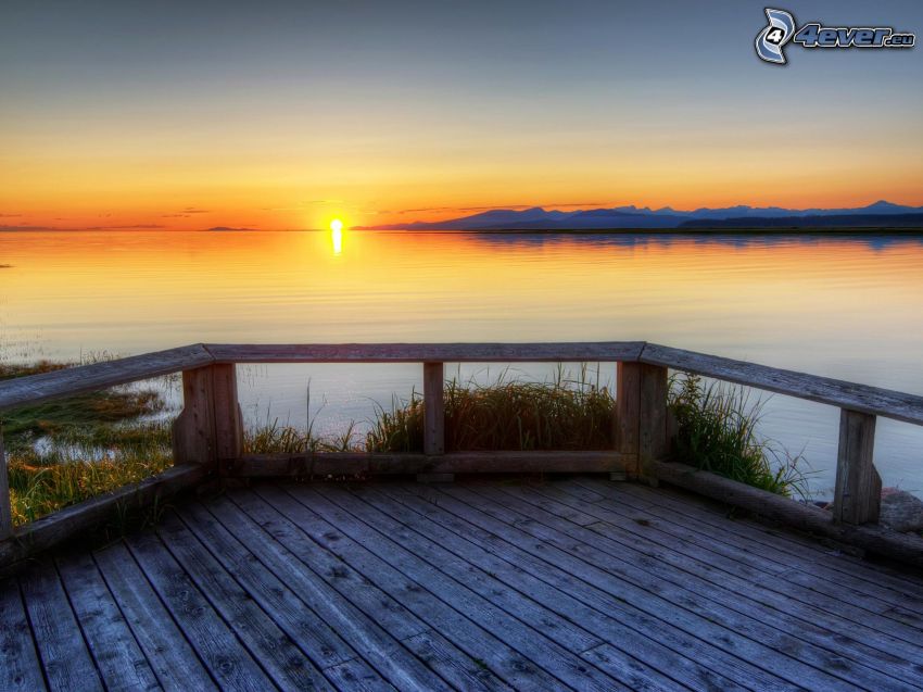 solnedgång bakom sjö, träbrygga