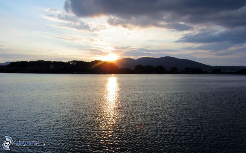 solnedgång över sjö, bergskedja, reflektion av solen