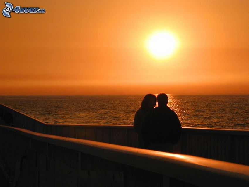 puesta de sol naranja sobre el mar, silueta de una pareja, romántica