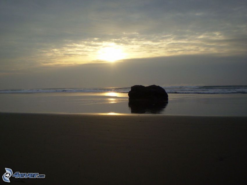 puesta de sol sobre el mar, roca en la playa