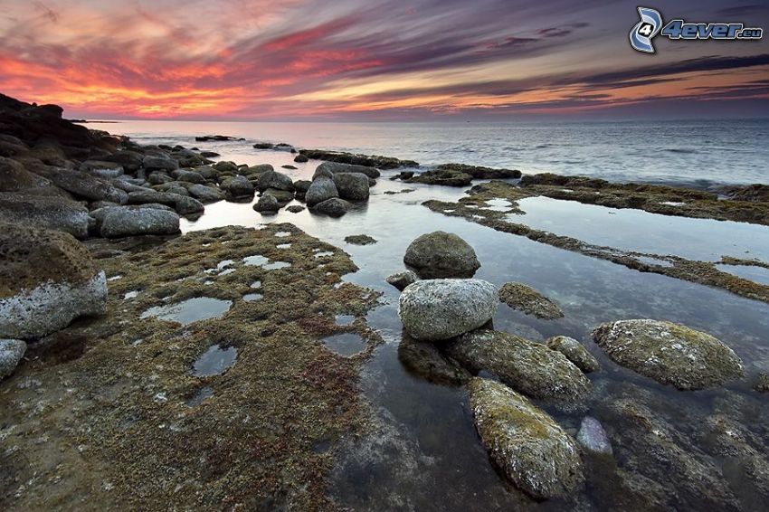puesta de sol sobre el mar, rocas en el mar, cielo de color rosa