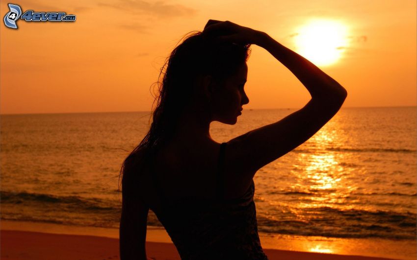 siluetta di donna al tramonto, tramonto sul oceano, cielo arancione