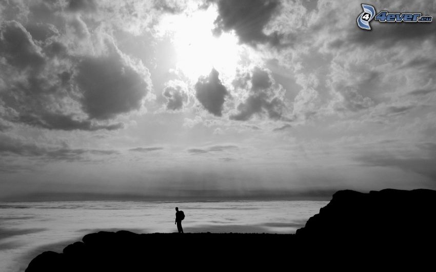 silueta chlapa, more, slnečné lúče za oblakom, čiernobiele