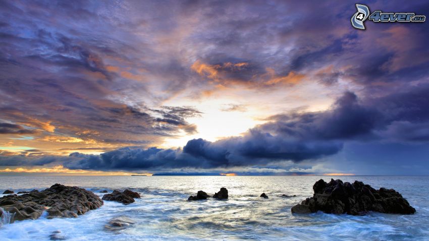 kamenistá pláž, západ slnka nad morom, tmavé oblaky