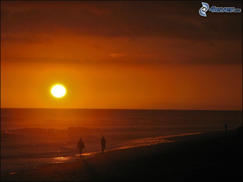 oranžový západ slnka nad morom, siluety ľudí, večerná pláž