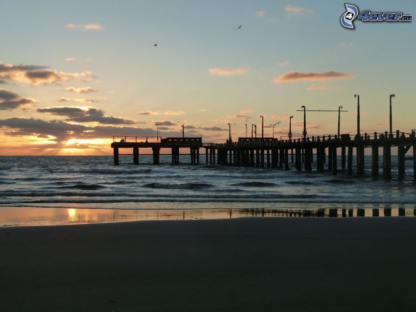 wooden pier, beach, sunset behind the sea