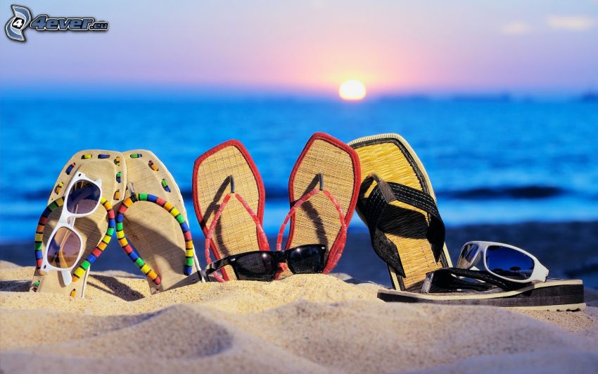 sandals, sand, sunglasses, sunset behind the sea
