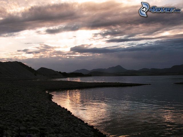 sunset over the lake, rocky coastline, hills, sun behind the clouds