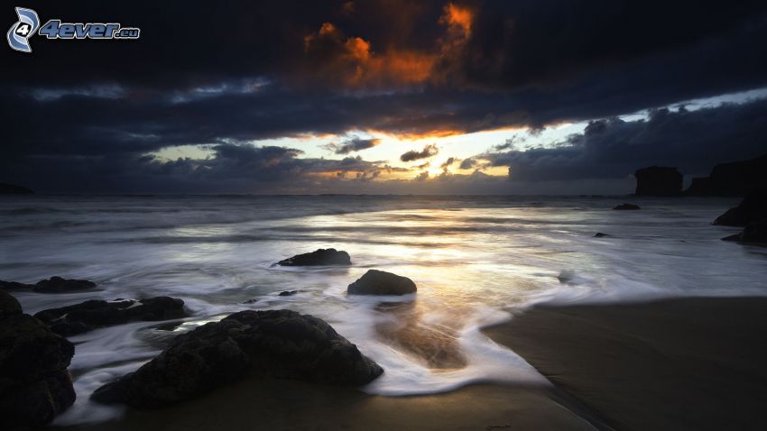 dark clouds above the beach, sea, sun, rocks
