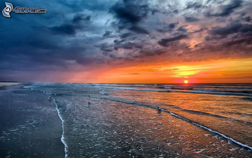 sunset behind the sea, sandy beach, dark clouds